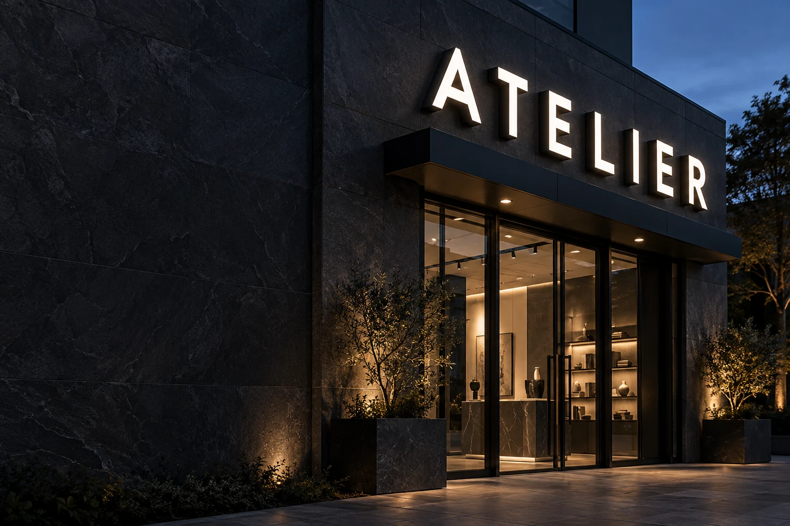 White front-lit ATELIER channel letters above a modern dark stone storefront at dusk