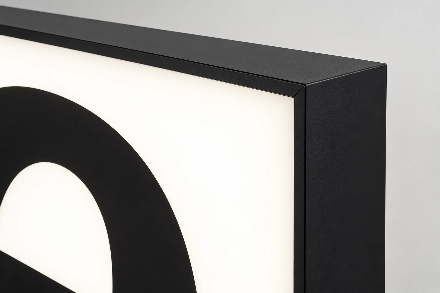 Close view of a lightbox corner showing a matte black frame, illuminated acrylic face and deep side return