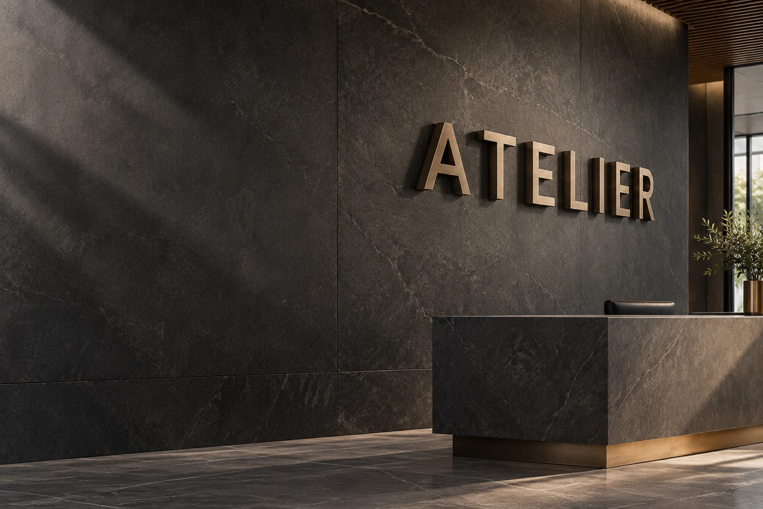 Brushed bronze ATELIER metal letters on a dark stone reception wall above a minimalist desk